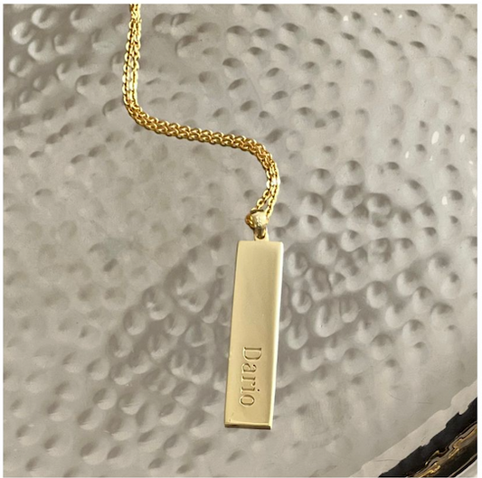 Gold necklace with a rectangular pendant on a textured gray background
