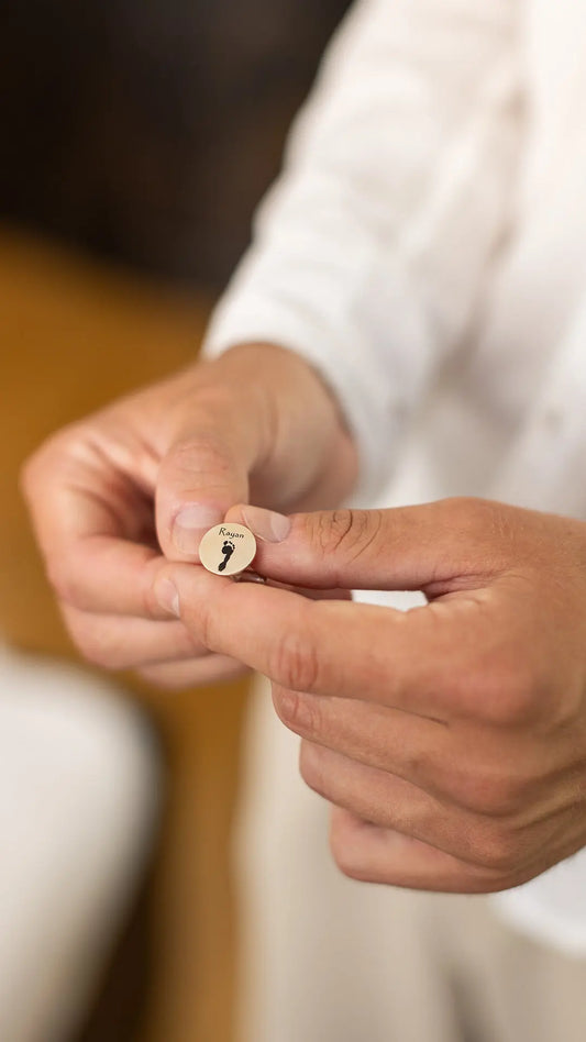 Engraved handprint and footprint cufflinks with black ink — handcrafted personalized jewelry. A man holding it in his hand