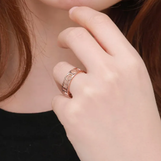 Close-up of a hand wearing the Amora Ring – Thin in rose gold, showcasing the delicate Roman numeral cutout design on the finger for an elegant everyday look.