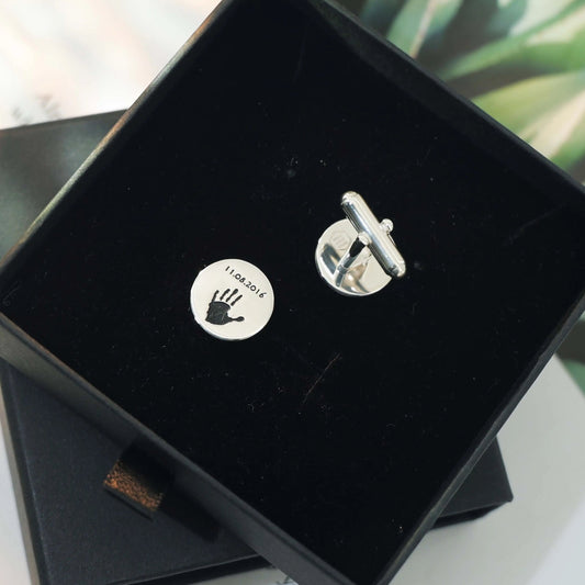 Round silver cufflinks engraved with a baby handprint and footprint inside a black gift box — personalized cufflinks by Chapters of Joy.