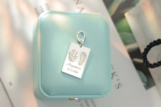 Sterling silver Ema Tag engraved with a child’s hand and footprint, name and birthdate attached to a keychain, symbolizing love and connection.