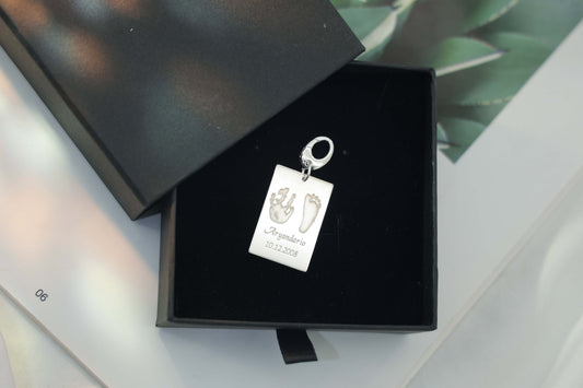 Sterling silver Ema Tag engraved with a child’s hand and footprint, name and birthdate attached to a keychain, symbolizing love and connection.