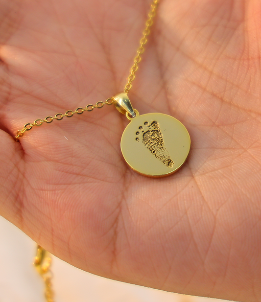 Gold necklace with a round pendant held in a hand against a light background
