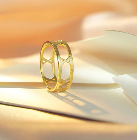 Amora Ring – Thin Roman numeral ring in 18k gold plating standing upright on a soft cream envelope with warm golden lighting, showcasing the delicate open-band design and elegant silhouette.