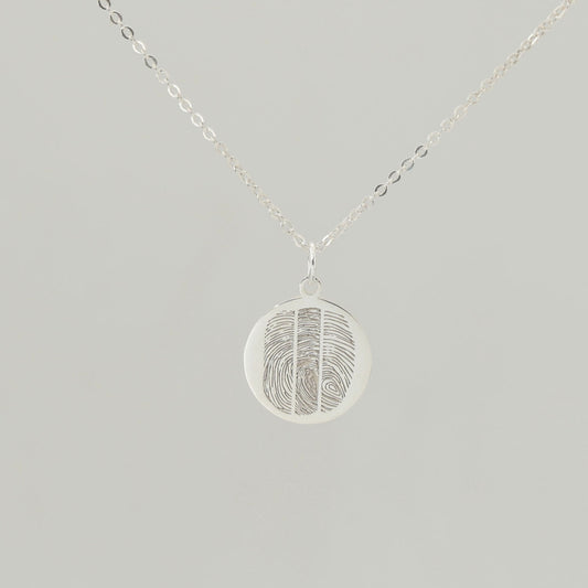 Sterling silver round fingerprint necklace with detailed engraving on soft grey background