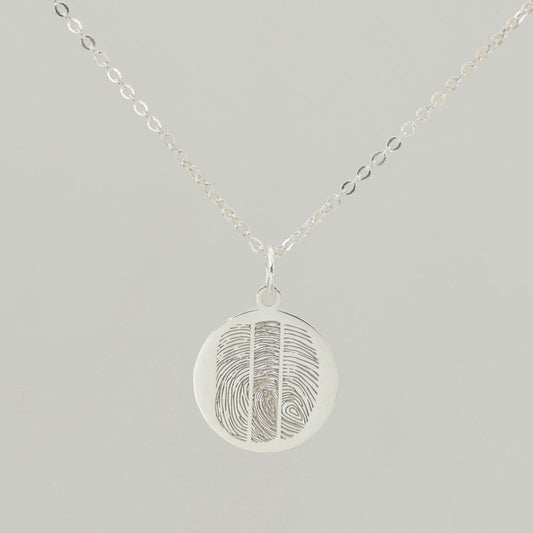 Sterling silver round fingerprint necklace with detailed engraving on soft grey background