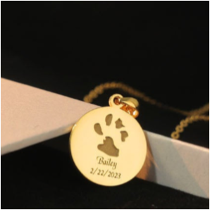 Gold necklace with a paw print pendant and engraved text on a black background