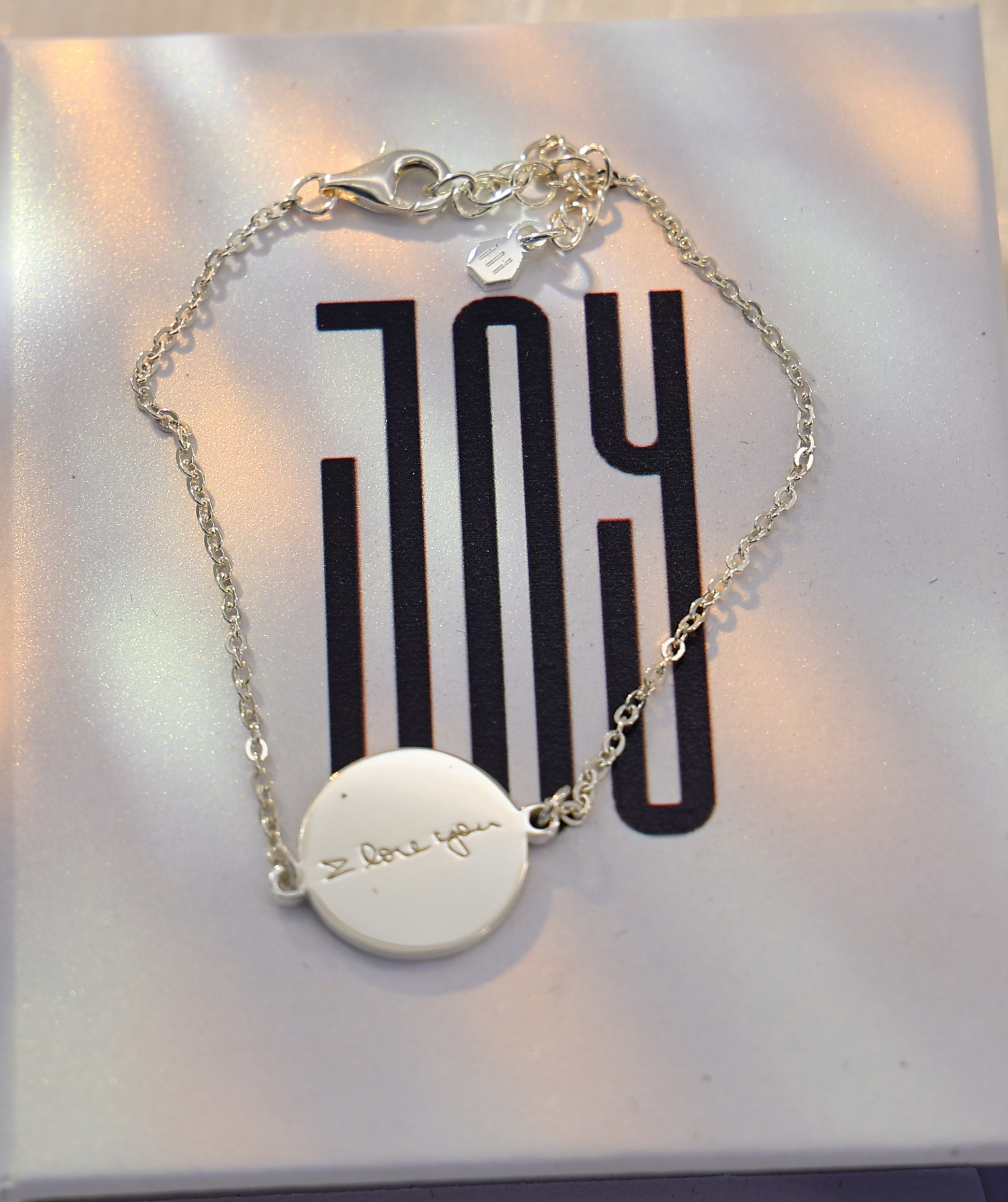 Personalized silver handwriting bracelet with round engraved charm reading “I love you,” displayed on a Chapters of Joy jewelry box.