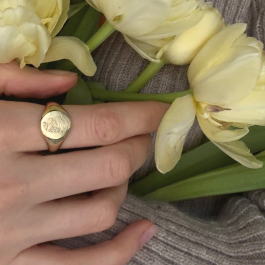 Custom gold signet ring worn on hand with flowers
