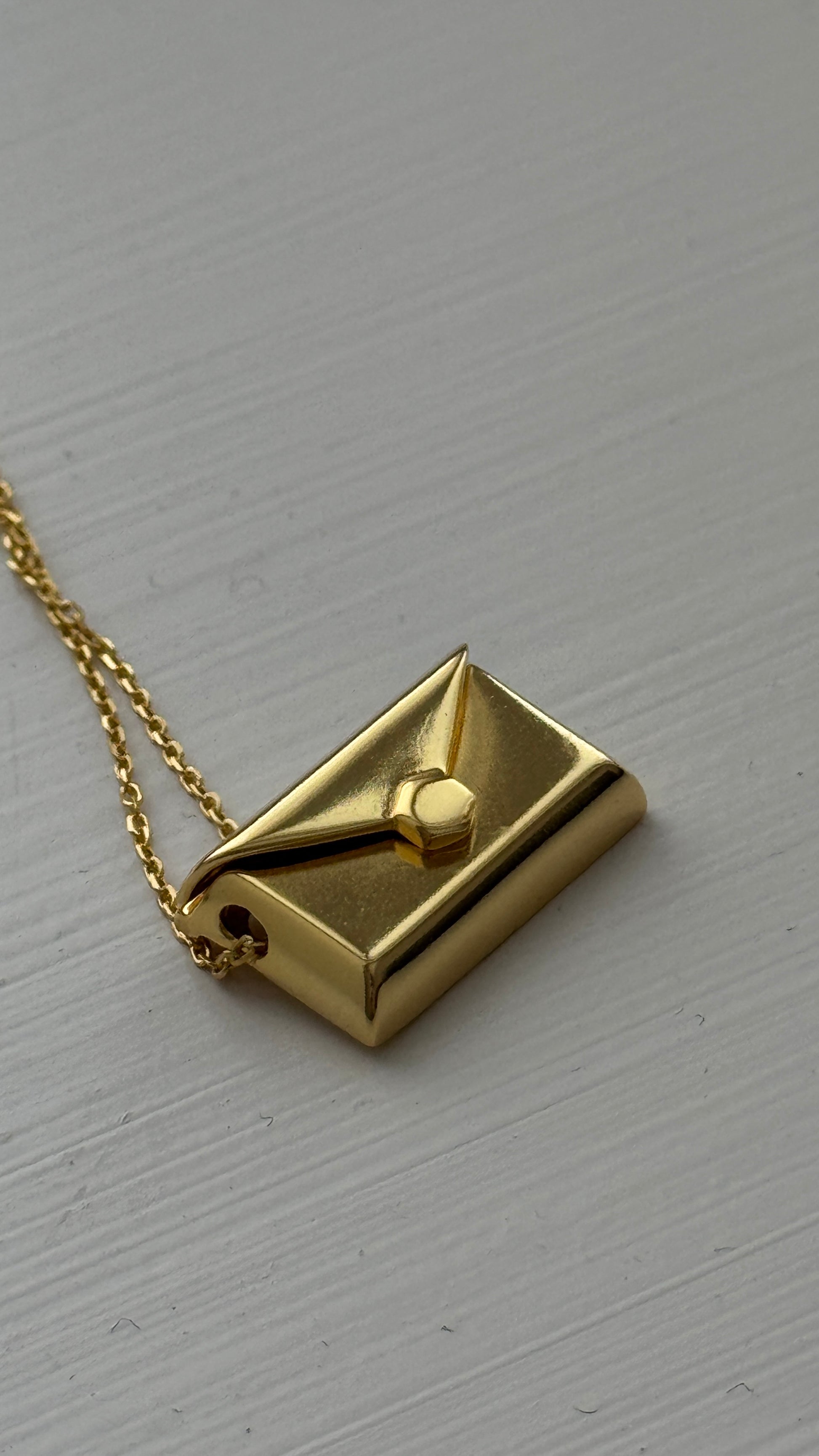 Gold envelope pendant that opens to reveal a hidden letter charm engraved with a personalized message.