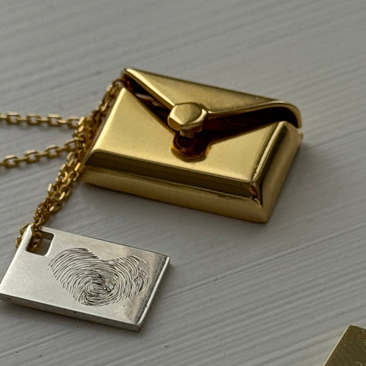 Gold plated envelope pendant that opens to reveal a hidden silver letter charm engraved with two finger prints in heart shape.