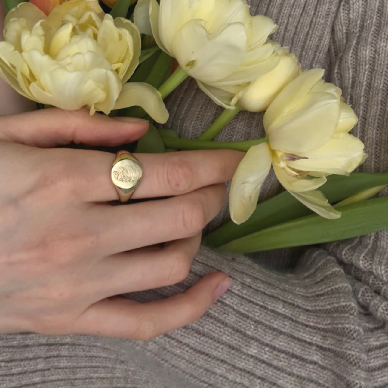 Hand wearing a gold plated signet ring with a fingerprint of her father engraved on it.
