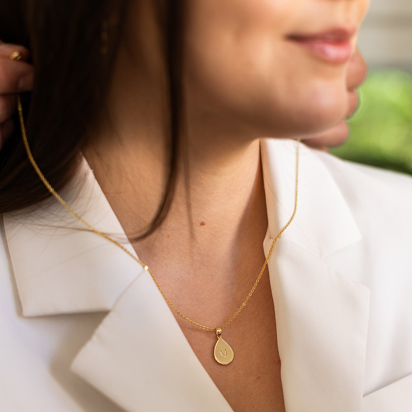 Close-up of a person wearing a gold necklace with a teardrop pendant, Initial of her name engraved