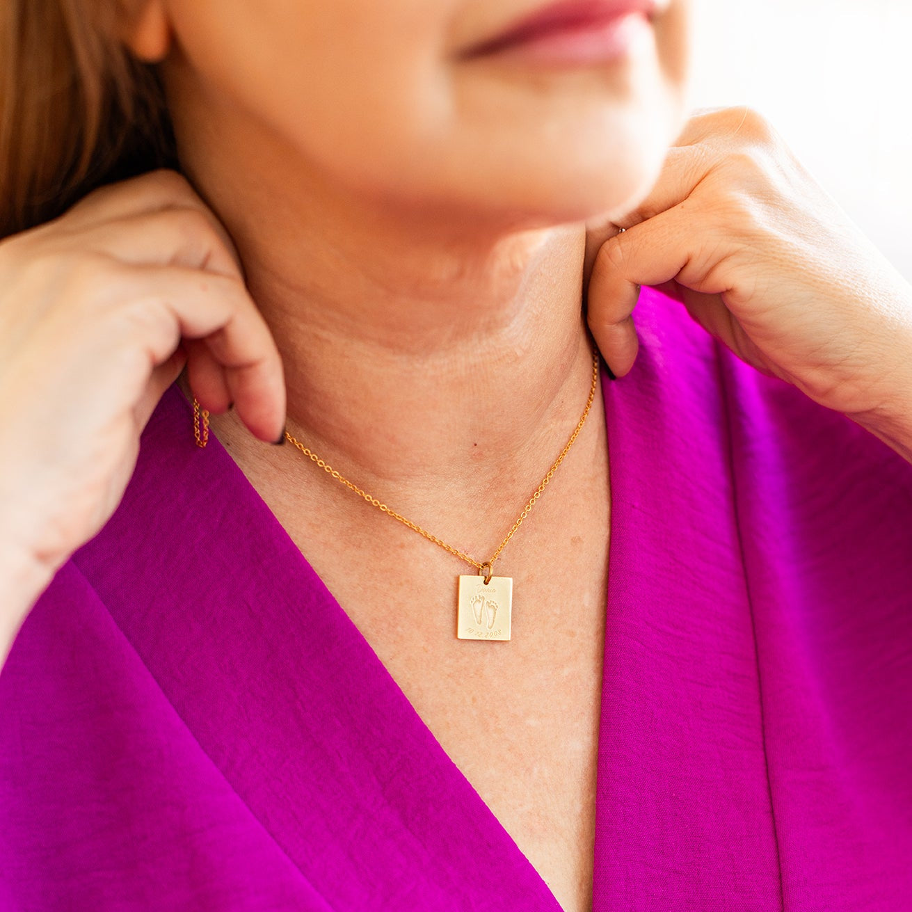 Person wearing a gold necklace with a square pendant with footprints of her baby engraved on it