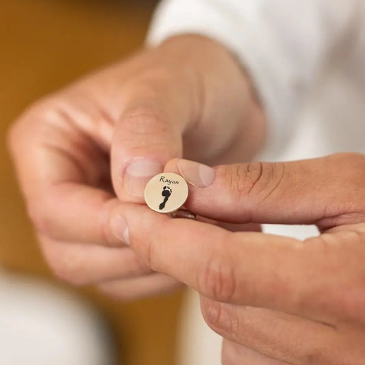 Person holding a personalized round cufflink engraved with a baby footprint — custom cufflinks by Chapters of Joy.