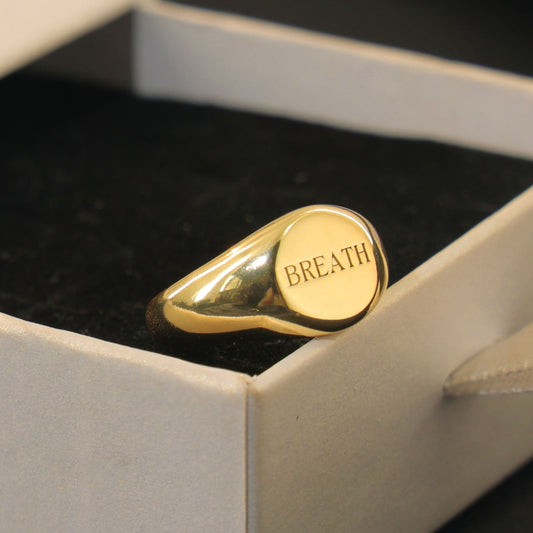 Round gold signet ring engraved with the word “BREATHE” by Chapters of Joy