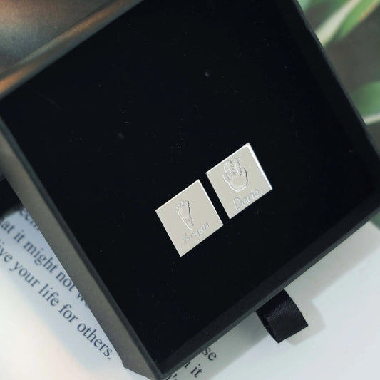 Square silver cufflinks engraved with a baby handprint and footprint inside a black gift box — personalized keepsake cufflinks by Chapters of Joy.