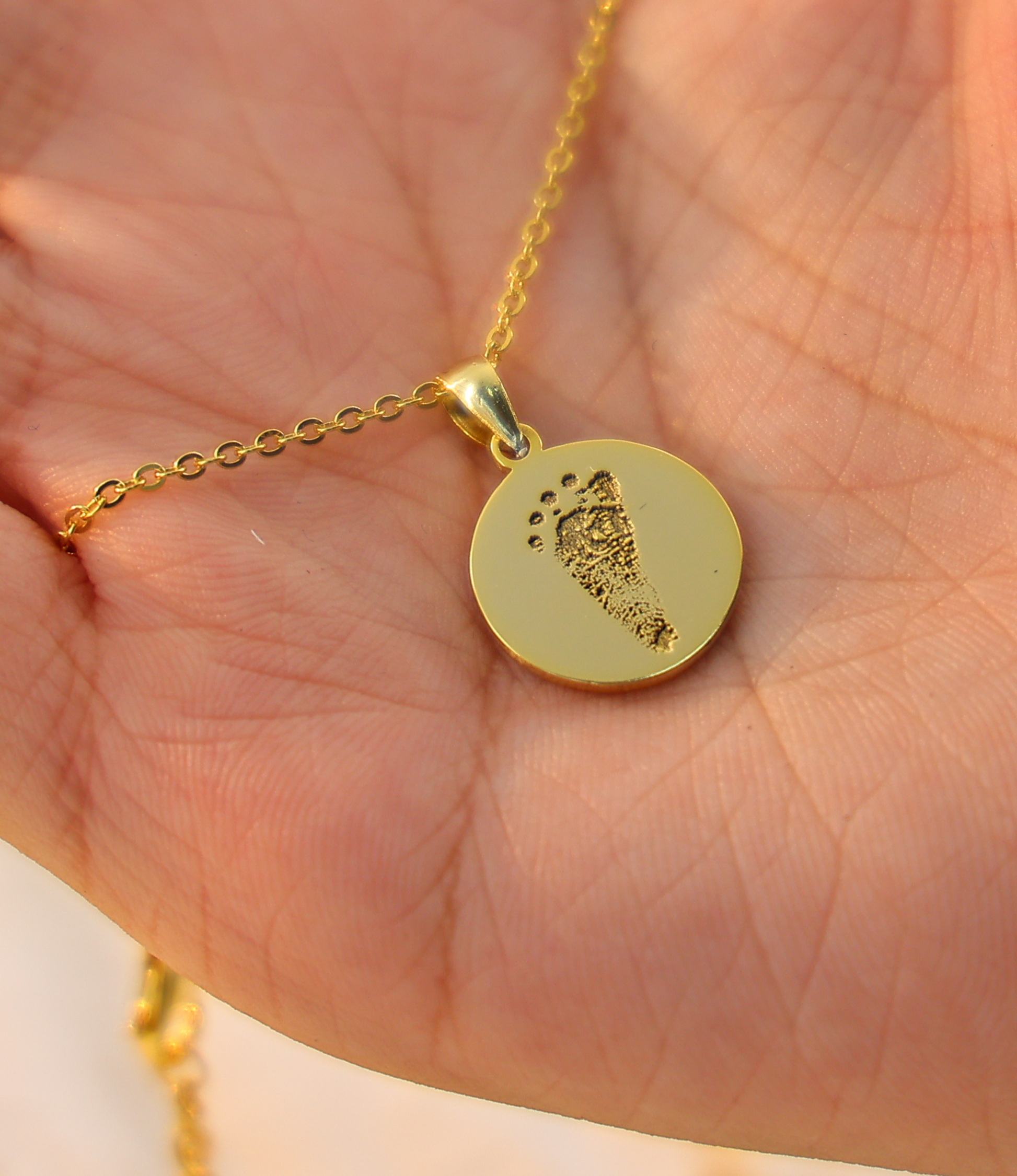 Gold necklace with a round pendant held in a hand against a light background