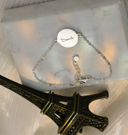 Personalized silver handwriting bracelet with round engraved charm displayed on a marble box beside a miniature Eiffel Tower decoration.