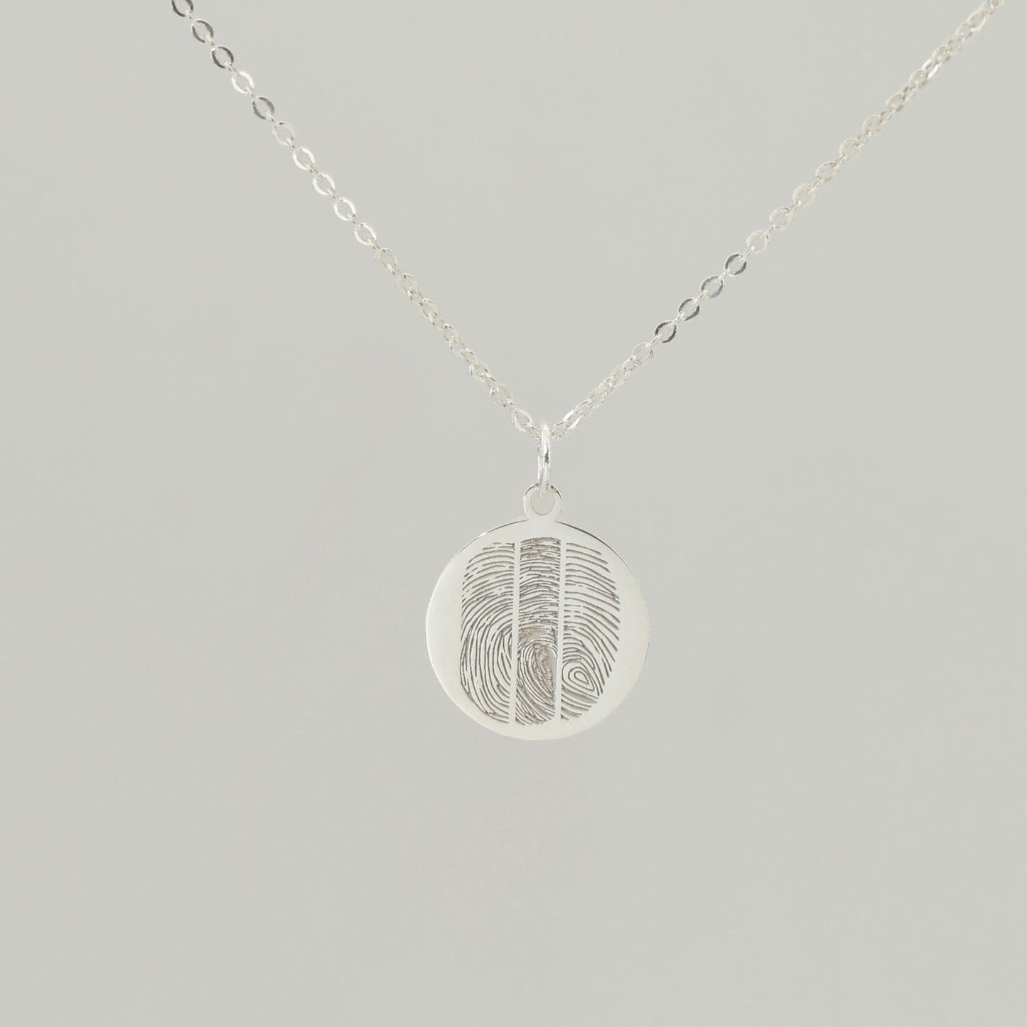 Sterling silver round fingerprint necklace with detailed engraving on soft grey background