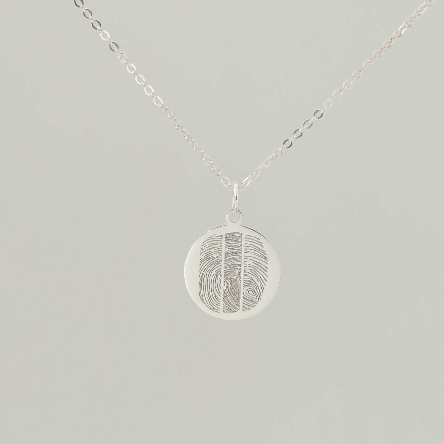 Sterling silver round fingerprint necklace with detailed engraving on soft grey background