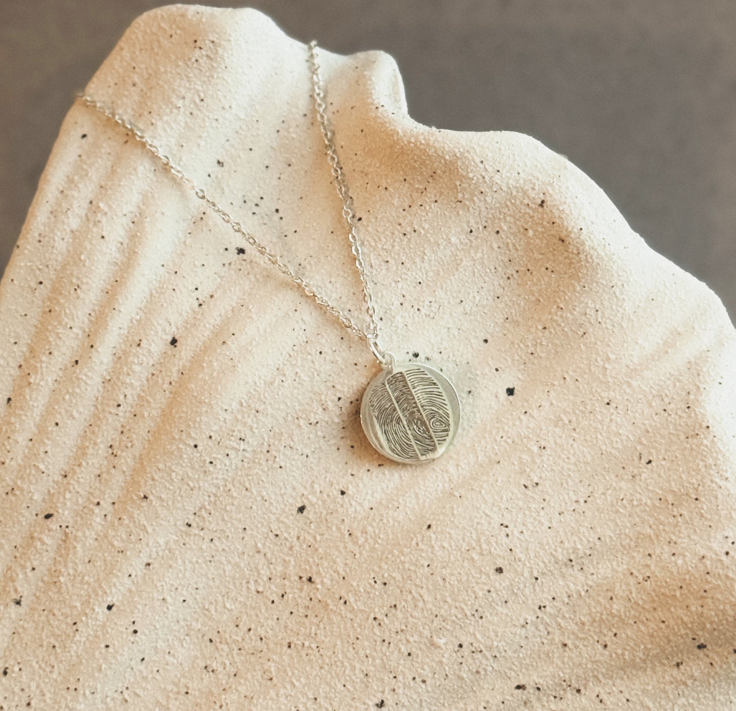 Round fingerprint pendant necklace in sterling silver on natural stone background