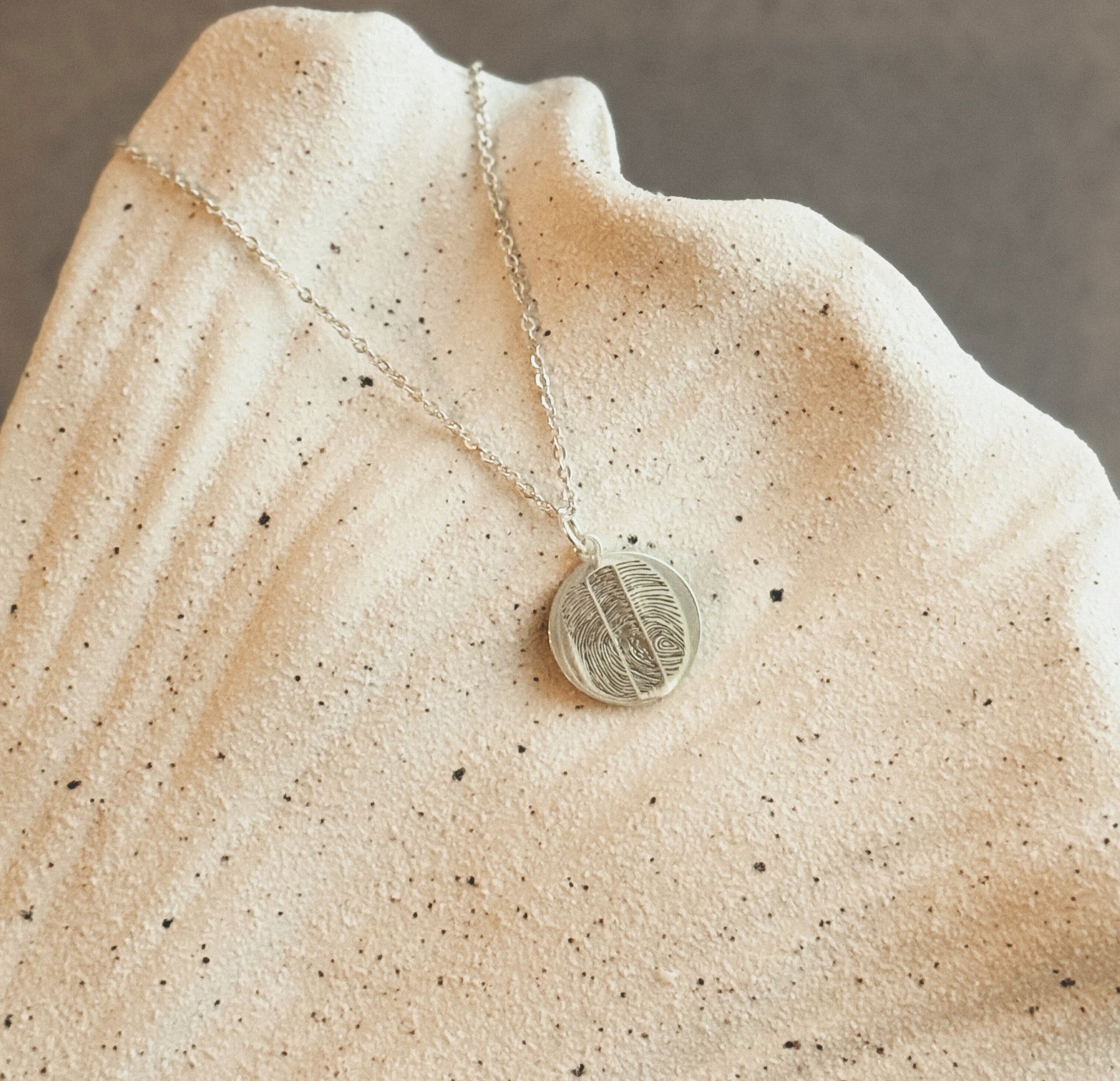 Round fingerprint pendant necklace in sterling silver on natural stone background